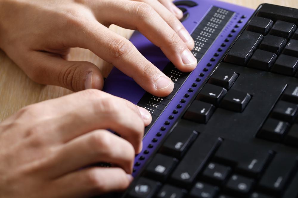 Hands typing on a purple braille keyboard
