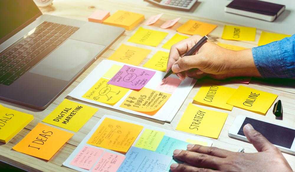 Hands writing on a table with several post-it notes with various words written on them