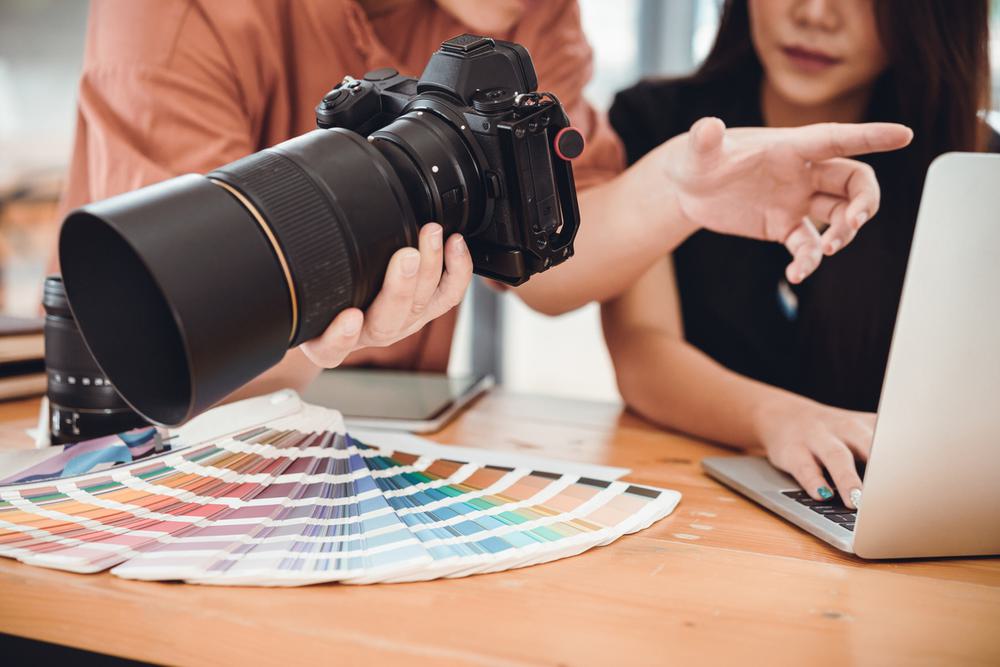 Two photographers, one holding a camera, discuss creative with a Pantone swatch book.