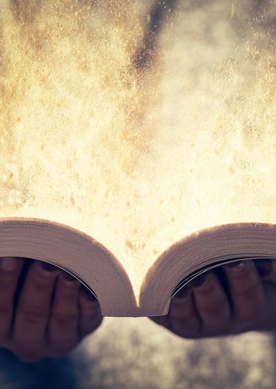 Hands holding an open book that emanates light