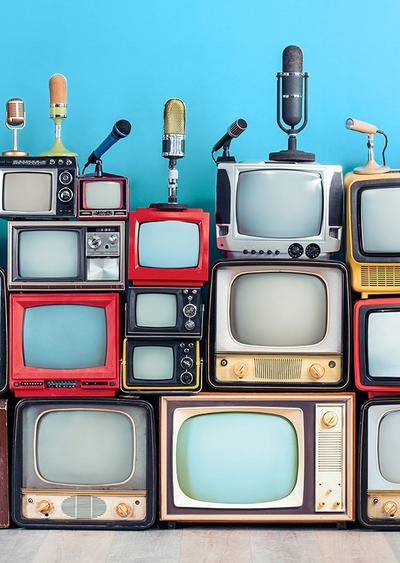 An assortment of retro TV sets and microphones stacked in front of a blue wall