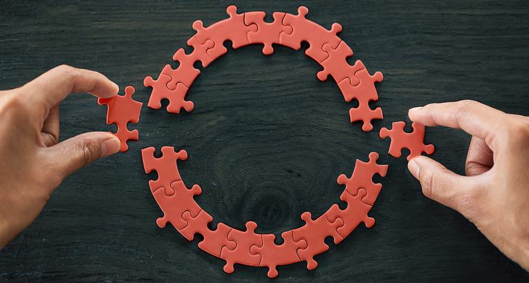 Two hands putting together a circular puzzle with red pieces