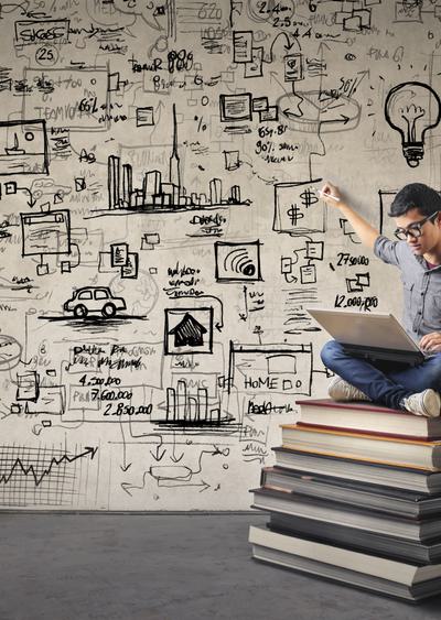 Student sitting on a stack of book with a laptop making graphics on wall